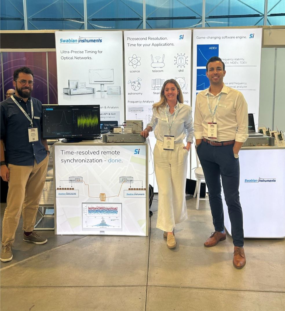 Swabian Instruments Team Members standing in front of the Swabian Instruments EFTF booth, with a live demonstration of ADEV, MDEV, and HDEV across 4 oscillators.
