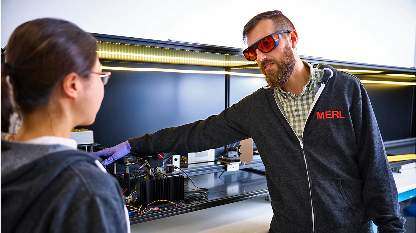 Joshua Rapp (right) points to the LiDAR experimental setup, discussing with Yanting Ma (left).
