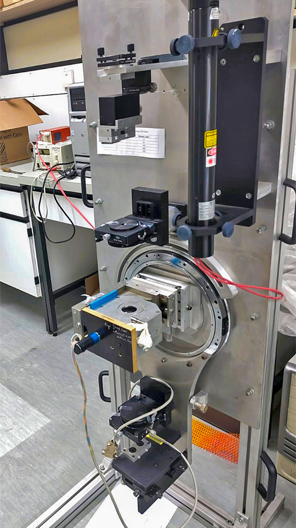 The image shows the custom echo DLS setup in the lab at the University of Stuttgart, consisting of a precision motor, a flat bearing, a thermal jacket, lenses, beam splitters, PMTs, a spectrometer, and Swabian Instrument’s Time Tagger 20.