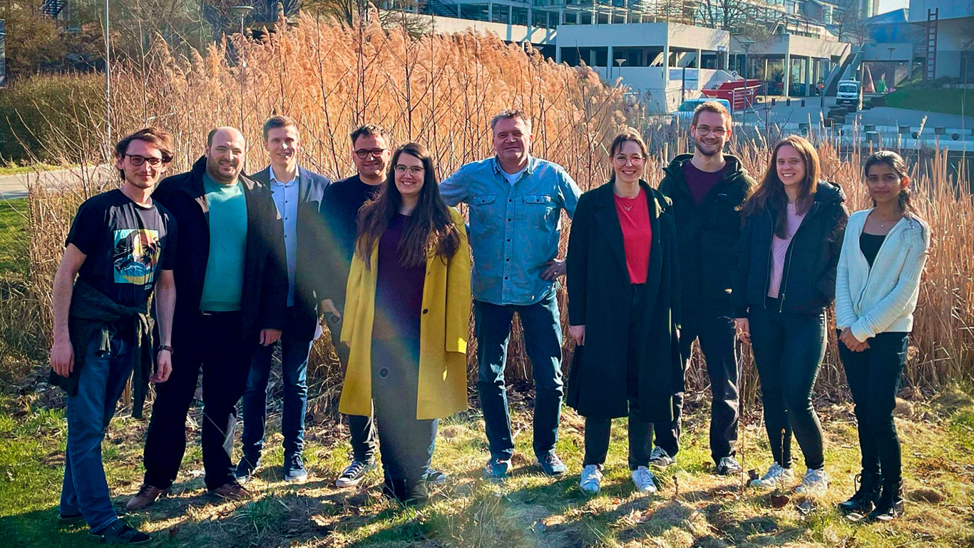 The image shows Prof. Thomas Sottman's group in the Department of Physical Chemistry at the University of Stuttgart, with the university building in the background.