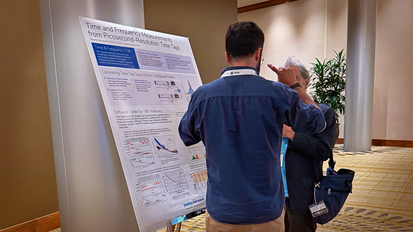 Edoardo Mornacchi standing in front of the poster for the presentation, 'Swabian Instruments’ software toolkit for time & frequency analysis,' explaining the measurements to another conference attendee.
