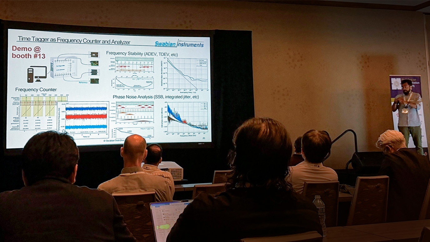 Edoardo Mornacchi standing in front of his presentation on Swabian Instruments’ software toolkit for time & frequency analysis. The slide demonstrates the following measurements, which users can perform simultaneously in real time: phase noise analysis, frequency stability analysis, frequency counting, and 1 PPS monitoring.