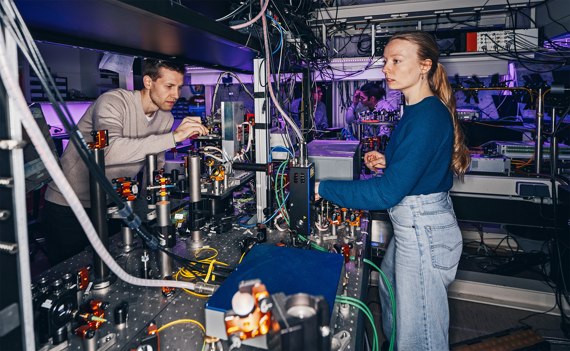 Lennart Jehle and his colleague Lena Hansen standing at their lab bench, which has their experimental setup used for investigating single-photon sources. © Ian Ehm
